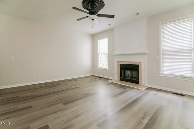 a view of an empty room with wooden floor fireplace and a window