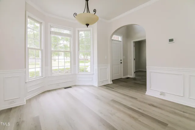 an empty room with wooden floor chandelier and windows