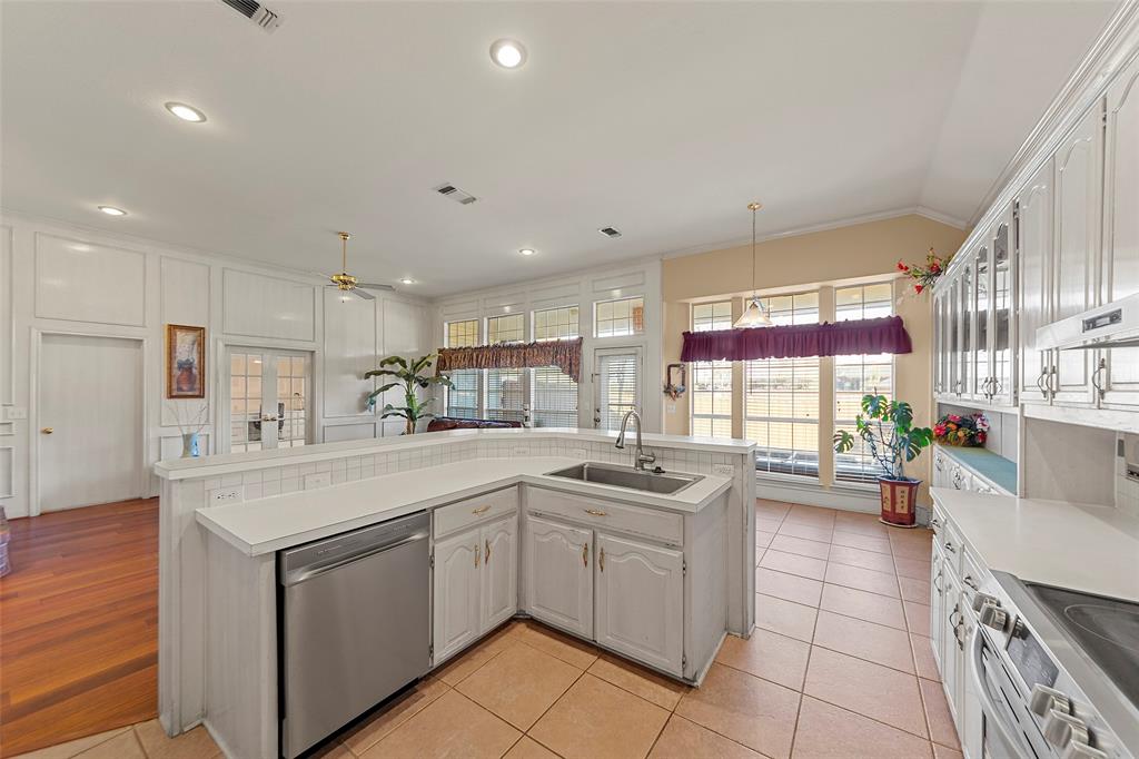 3308 North Spring Drive Richardson, TX 75082 - Photo 12 of 38 The spacious kitchen offers abundant cabinetry and generous counter space, making it both functional and inviting. A large center island with built-in sink overlooks the living area, creating an ideal layout for everyday living and effortless entertaining. Recessed lighting and light-filled walls enhance the bright, open feel, while the tile flooring adds durability and easy maintenance. With ample storage and a seamless connection to the family room, this kitchen is designed for comfort, convenience, and gathering.