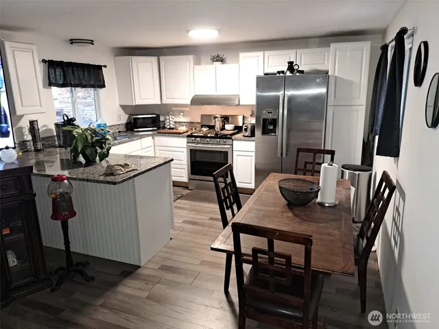 a kitchen with stainless steel appliances granite countertop a dining table chairs refrigerator and sink