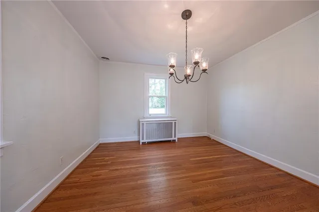 a view of empty room with wooden floor chandelier and window