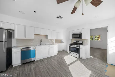 a kitchen with stainless steel appliances a stove a sink dishwasher a refrigerator and white cabinets with wooden floor