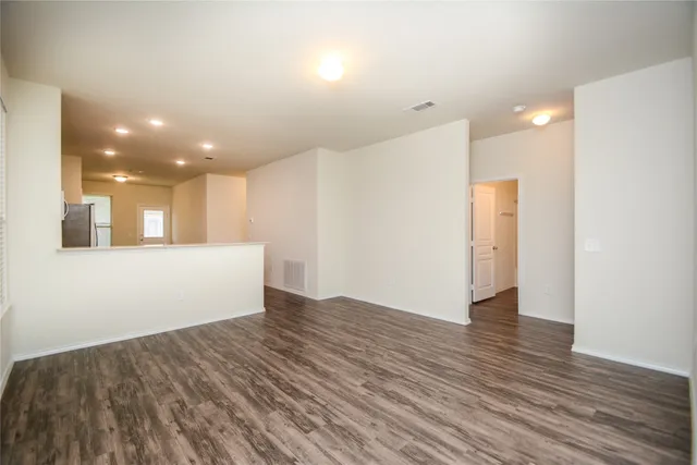 a view of an empty room with wooden floor and a kitchen