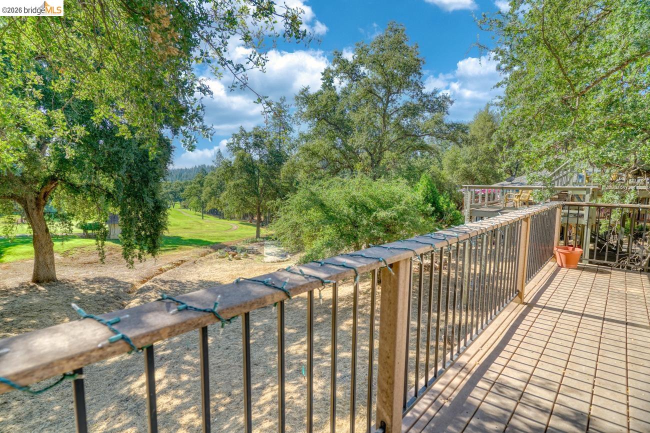 19215 Ferretti Road Groveland, CA 95321 - Photo 30 of 40 Wood-finish deck with square tile pattern and metal railing, overlooking a sloped natural landscape with mature trees and green areas