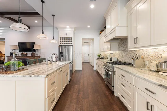a large kitchen with stainless steel appliances kitchen island granite countertop a sink a stove and a wooden floors