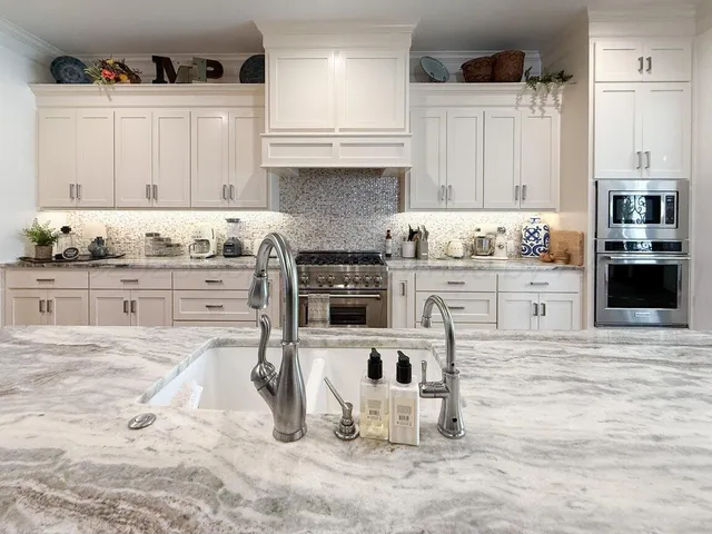 a kitchen with stainless steel appliances kitchen island granite countertop a stove a sink and white cabinets