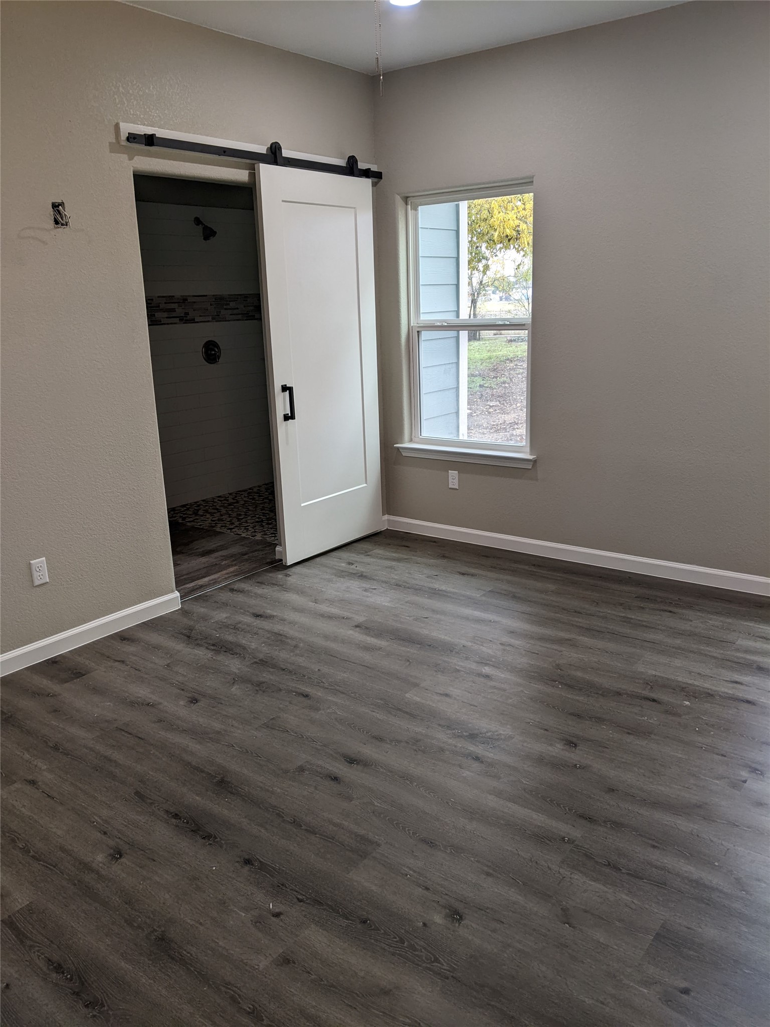 906 Kate Street, Unit A Lockhart, TX 78644 - Photo 8 of 15 Unfurnished bedroom featuring a barn door, a spacious closet, dark wood-style floors, and a ceiling fan, with walk in shower for the primary bathroom