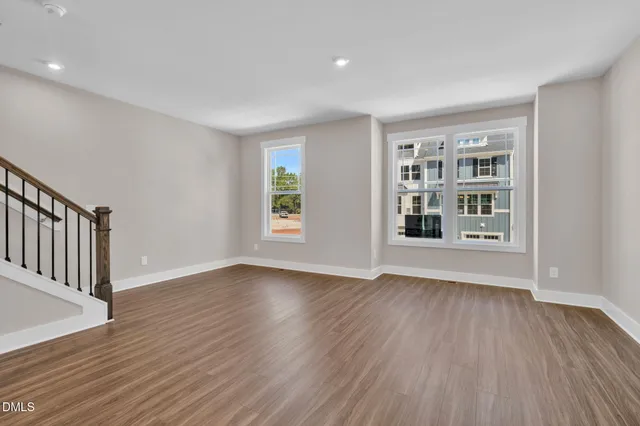 a view of an empty room with wooden floor stairs and a way to kitchen