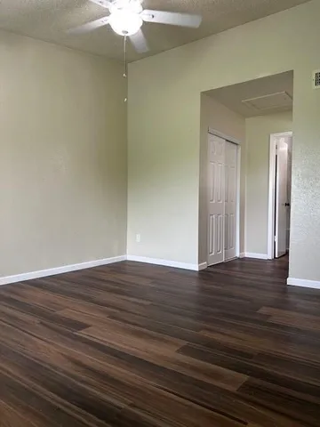 a view of an empty room with wooden floor and a fan