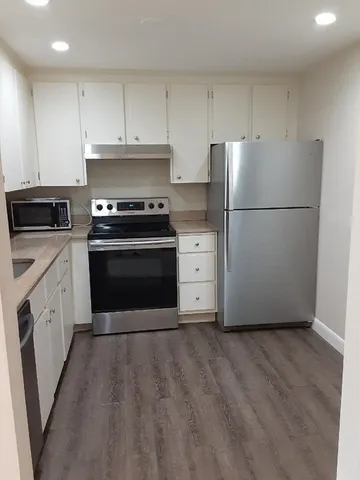 a kitchen with granite countertop a refrigerator stove and white cabinets
