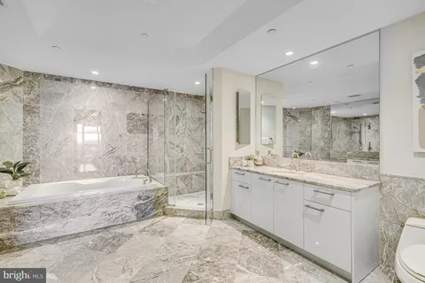 a bathroom with a granite countertop sink a toilet a large mirror and shower