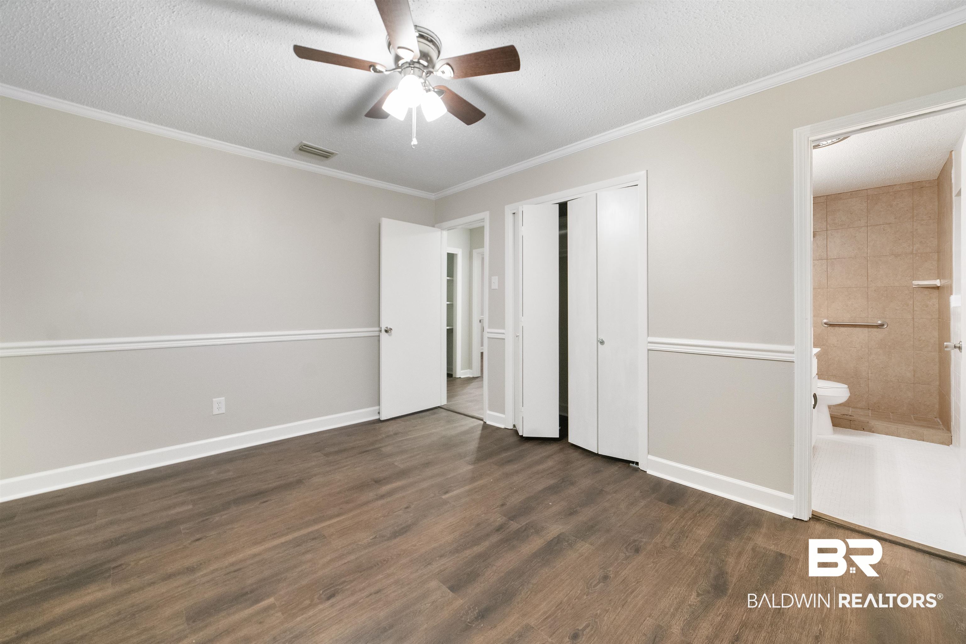 11833 Old Moffat Road Wilmer, AL 36587 - Photo 13 of 23 Unfurnished bedroom with a textured ceiling, connected bathroom, visible vents, dark wood-style floors, and crown molding