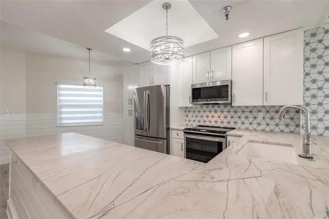 a kitchen with stainless steel appliances granite countertop a sink a stove a refrigerator cabinets and a dining table