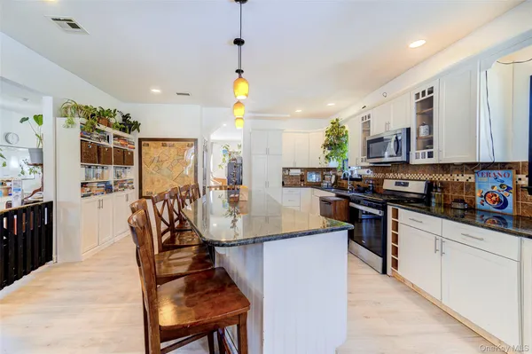 a kitchen with stainless steel appliances granite countertop a stove a refrigerator a kitchen island a dining table and chairs with wooden floor