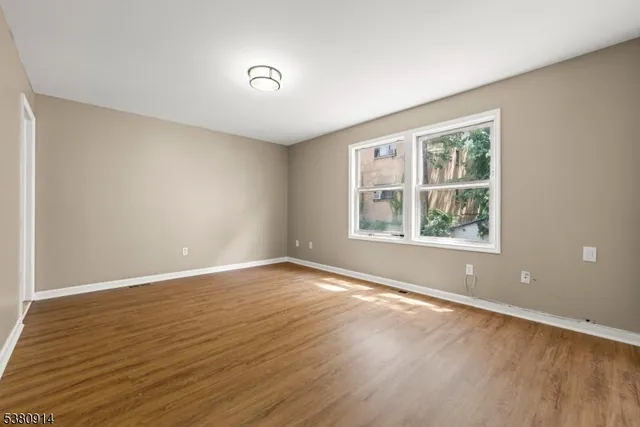 a view of an empty room with wooden floor and a window