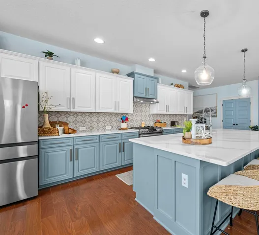 a kitchen with stainless steel appliances granite countertop a sink a stove a refrigerator and island with wooden floor