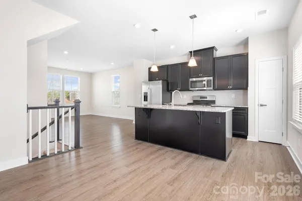 a kitchen with stainless steel appliances kitchen island granite countertop a refrigerator a sink dishwasher and a oven with wooden floor