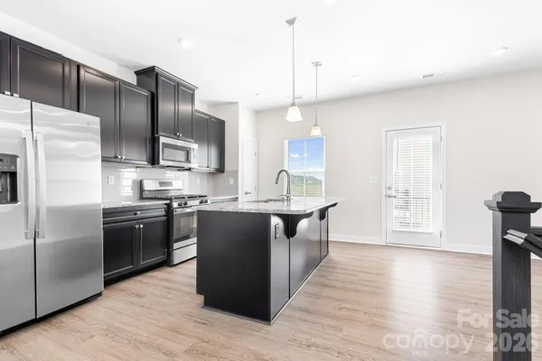 a kitchen with stainless steel appliances granite countertop a refrigerator a sink dishwasher a kitchen island with wooden cabinets and floors