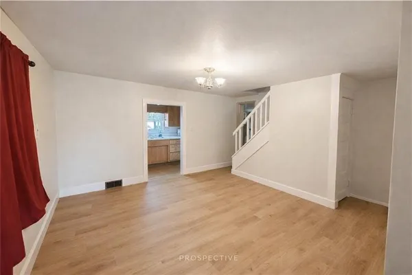a view of an empty room with wooden floor and kitchen