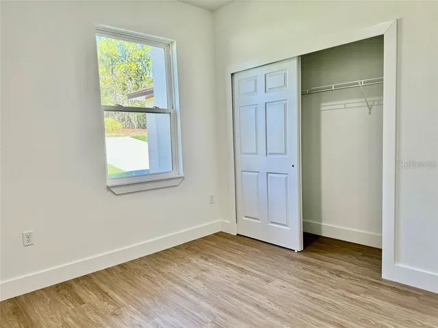 an empty room with wooden floor closet and windows