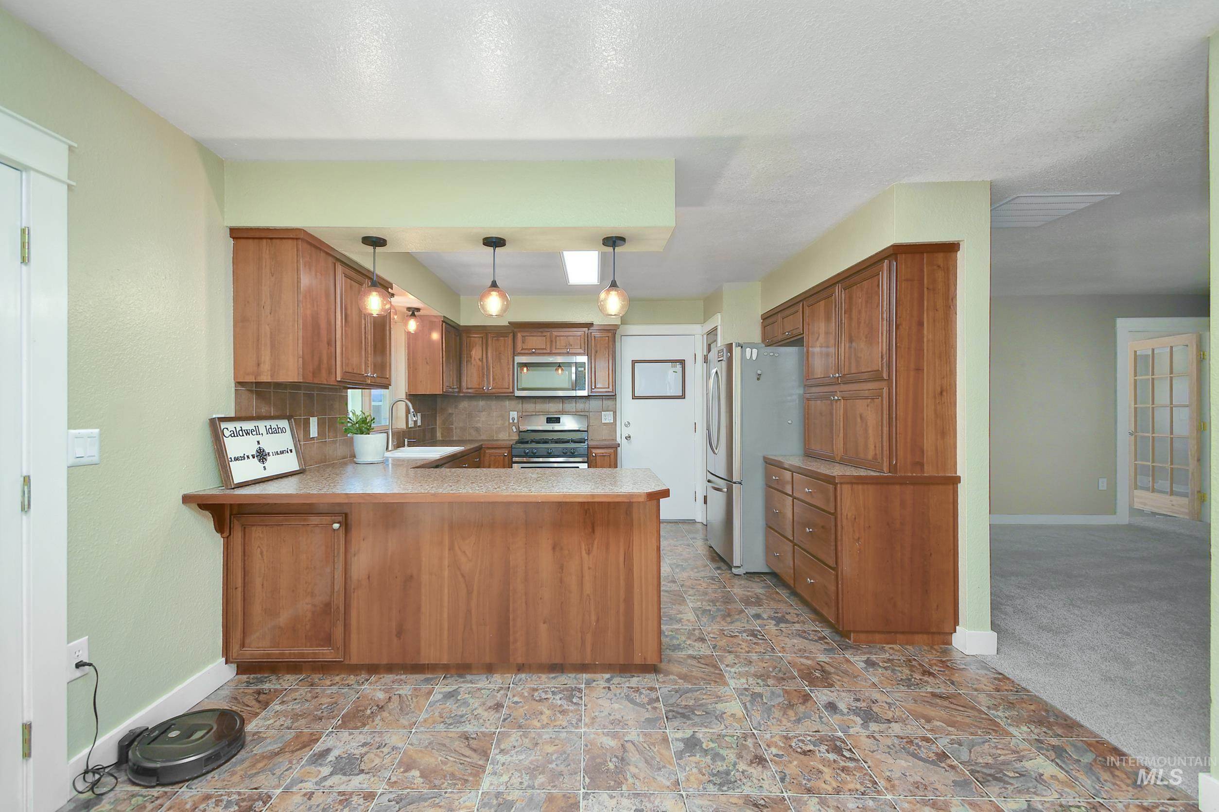 1108 East Ustick Road Caldwell, ID 83607 - Photo 7 of 30 Kitchen featuring wood-finish cabinetry, stainless steel appliances, a tile backsplash, and a breakfast bar