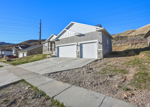 45 Memory Lane Tooele, UT 84074 - Photo 2 of 30 View of side of home with an attached garage, concrete driveway, stone siding, a mountain view, and stucco siding