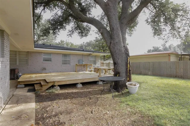 a view of a backyard with table and chairs potted plants and a large tree