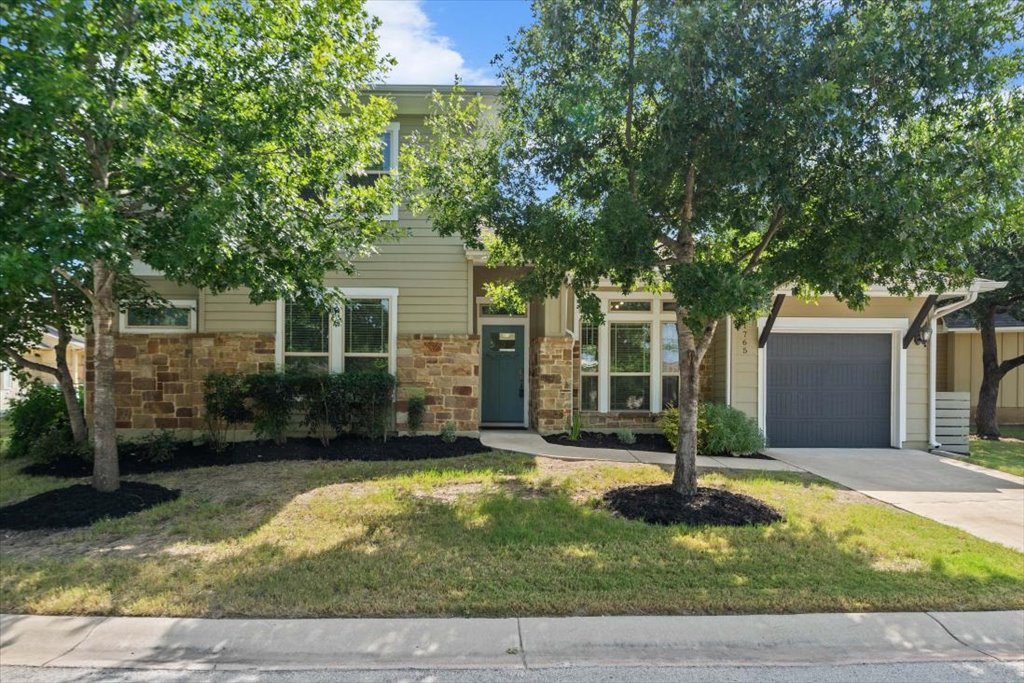 Mature trees shade a charming exterior combining horizontal siding with warm stone accents.