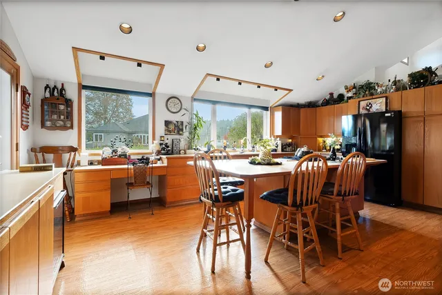 a dining hall with stainless steel appliances kitchen island granite countertop a table chairs and a wooden floor