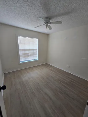 an empty room with wooden floor windows and fan