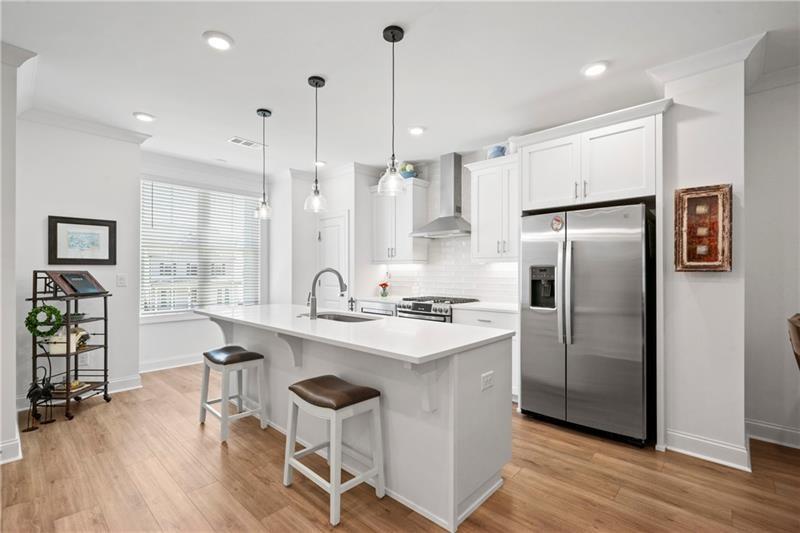 a kitchen with stainless steel appliances granite countertop a refrigerator a sink dishwasher a stove and white cabinets with wooden floor