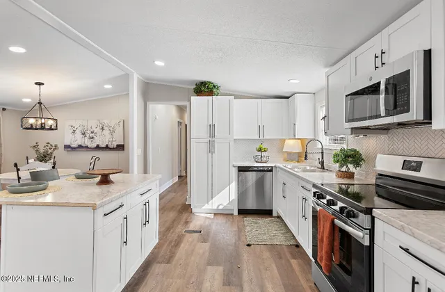 a kitchen with stainless steel appliances granite countertop a stove top oven a sink dishwasher and a refrigerator with wooden floor