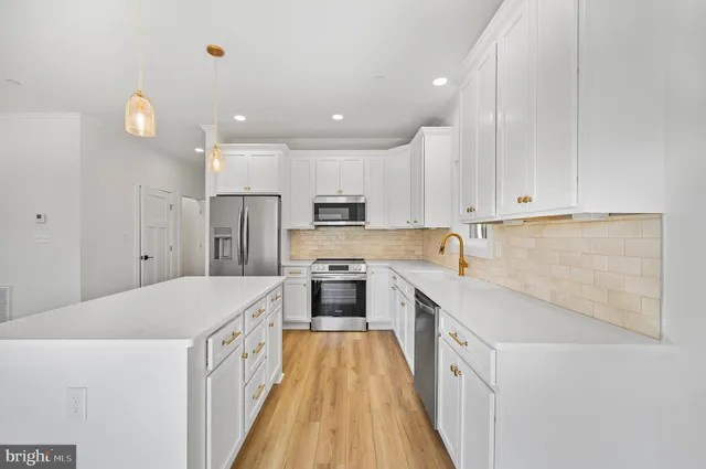 a large white kitchen with stainless steel appliances granite countertop a stove a sink a refrigerator and white cabinets with wooden floor