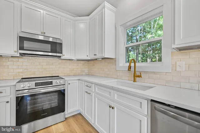 a kitchen with granite countertop white cabinets appliances and a window