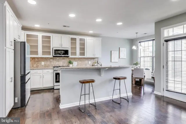 a kitchen with stainless steel appliances a microwave a stove a sink dishwasher a refrigerator and white cabinets with wooden floor