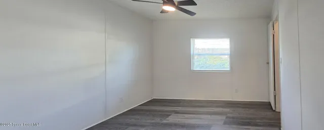 an empty room with wooden floor chandelier fan and windows