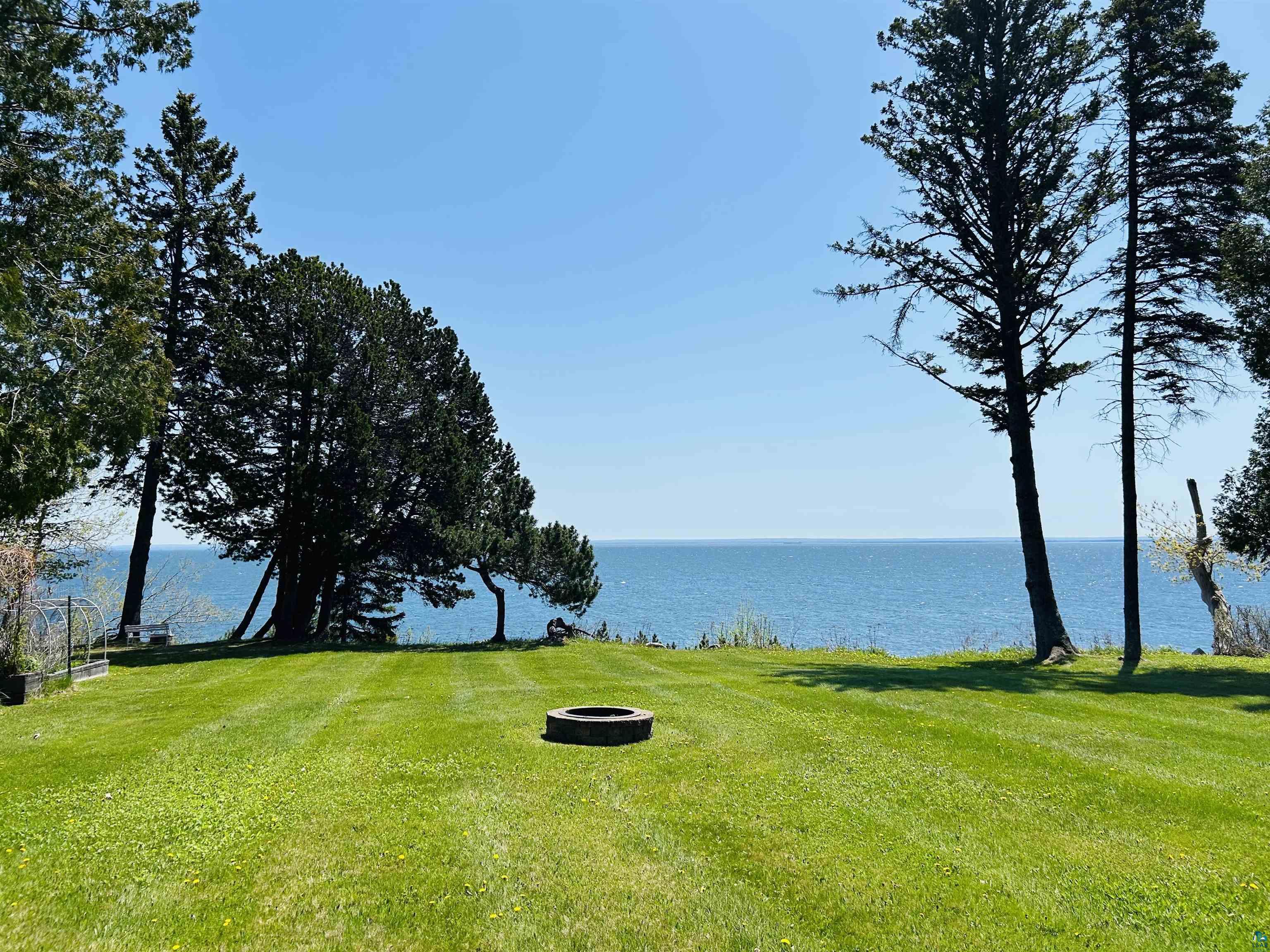 5090 London Road, Unit 1 Duluth, MN 55804 - Photo 41 of 54 Expansive waterfront lawn featuring a stone fire pit, mature evergreen trees, and clear water