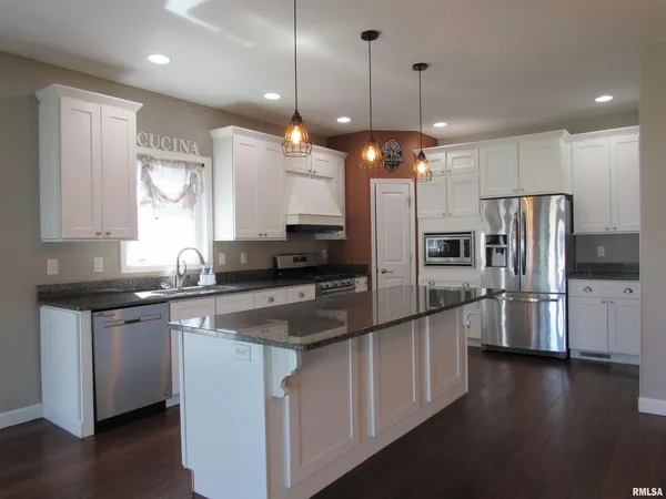 a kitchen with stainless steel appliances granite countertop a refrigerator a sink dishwasher a stove and white cabinets with wooden floor