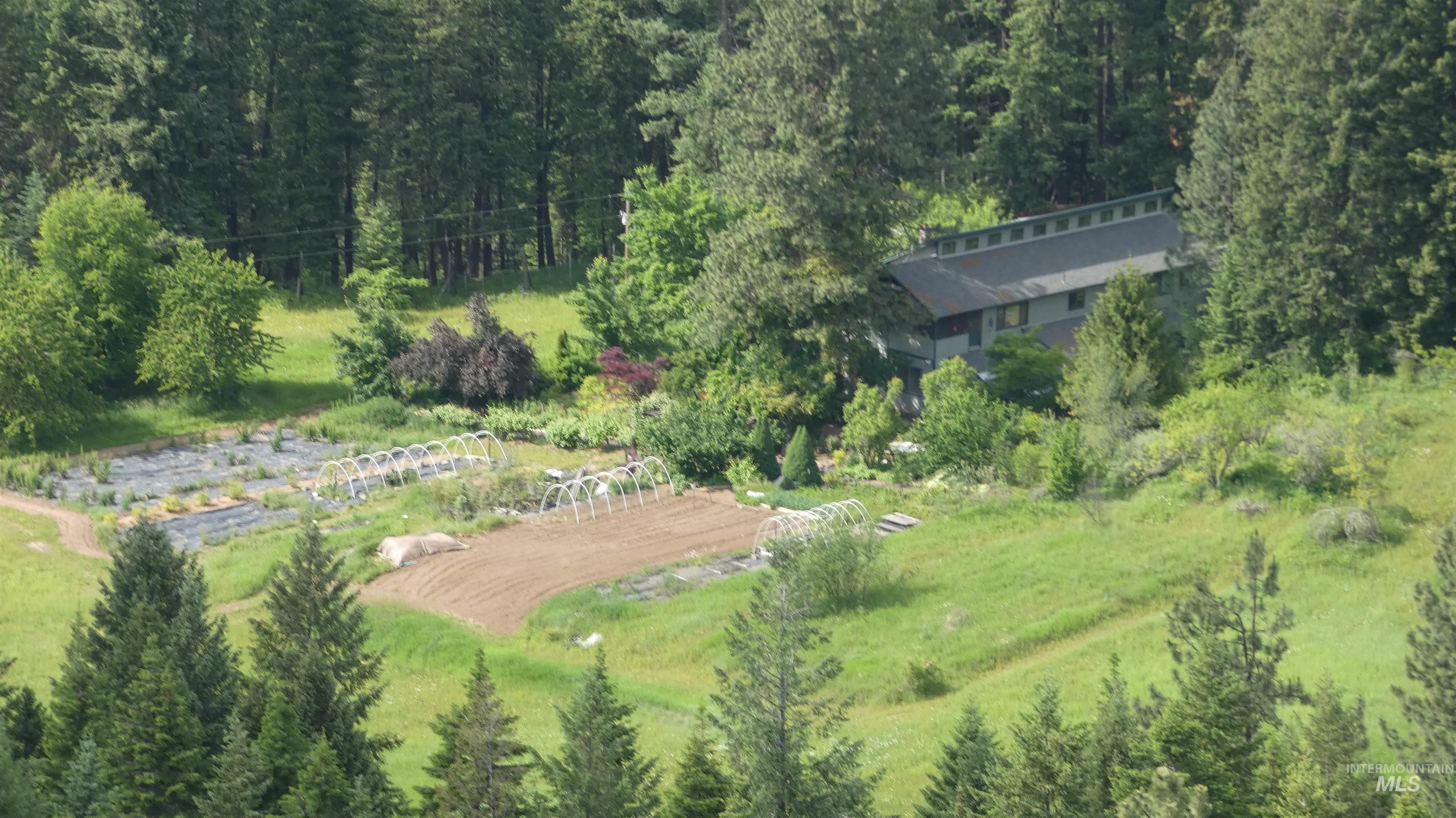 266 Falcon Ridge Road Kooskia, ID 83539 - Photo 45 of 50 Rural property featuring an extensive cultivated garden area with hoop structures, surrounded by mature evergreen and deciduous trees