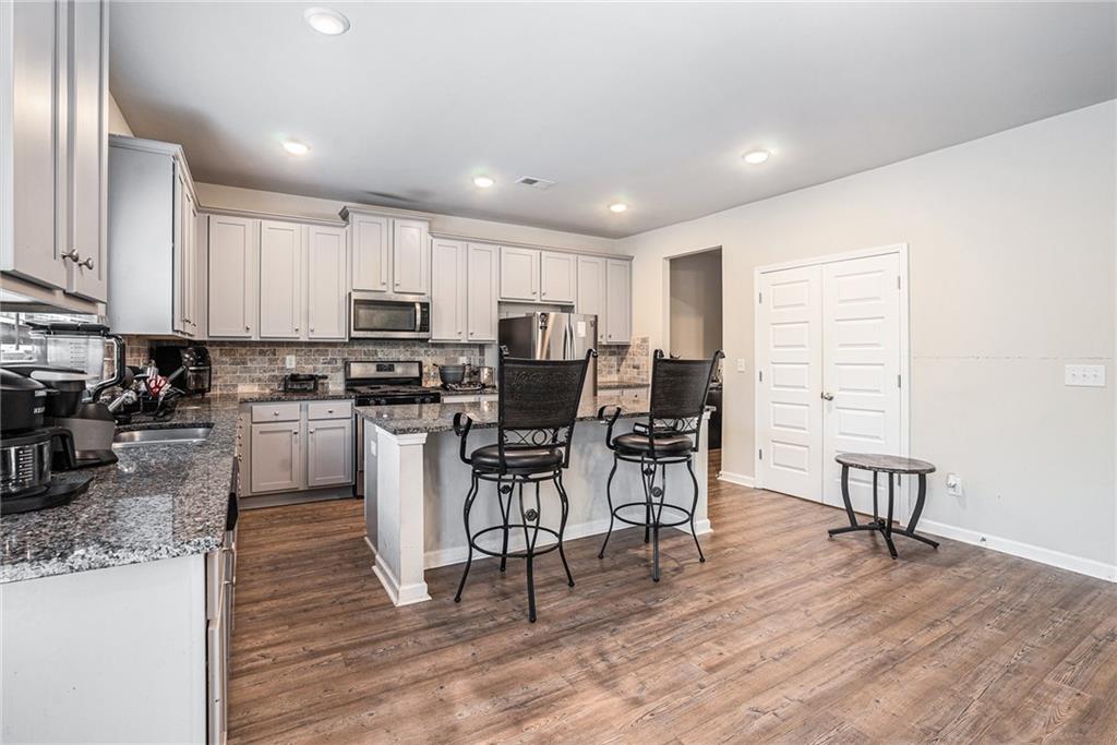 2428 Hanover Woods Road Lithonia, GA 30058 - Photo 8 of 26 a kitchen with stainless steel appliances granite countertop a stove top oven a sink a dining table and chairs with wooden floor