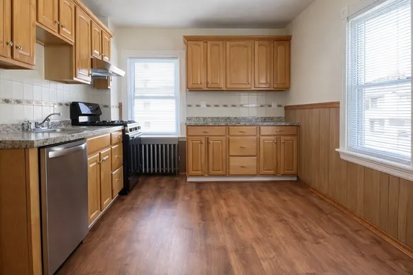 a kitchen with stainless steel appliances granite countertop wooden cabinets a stove a sink and dishwasher with wooden floor