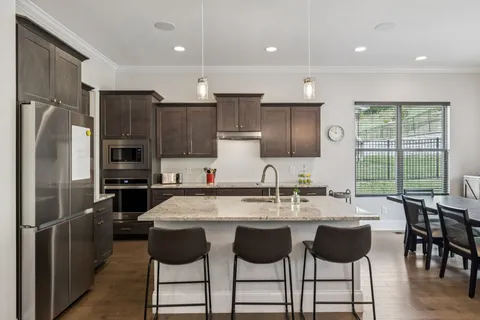 a kitchen with stainless steel appliances granite countertop a refrigerator a sink a stove a dining table and chairs