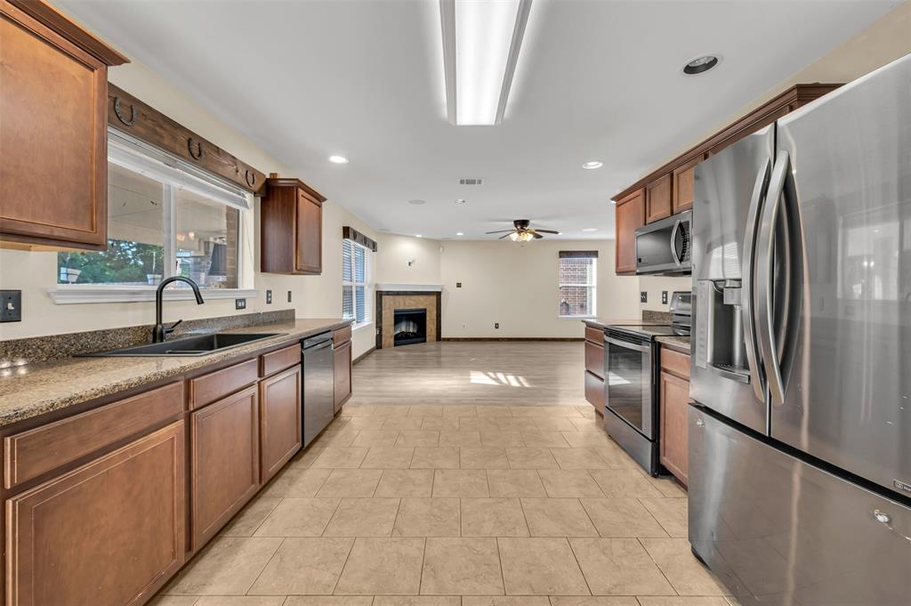 9017 Graywolf Ridge Trail Fort Worth, TX 76244 - Photo 11 of 27 Kitchen featuring light tile flooring, stainless steel appliances, ceiling fan, sink, and a tile fireplace