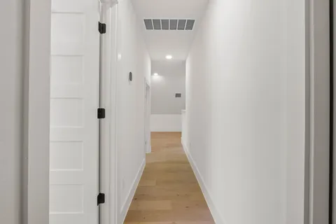 a view of a hallway with wooden floor and a bathroom