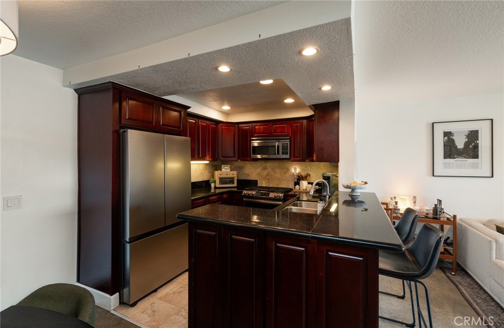 8512 Tuscany Avenue, Unit 222 Playa del Rey, CA 90293 - Photo 2 of 24 a kitchen with stainless steel appliances granite countertop a refrigerator a sink a stove a dining table and chairs