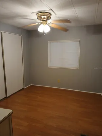 an empty room with a chandelier fan and wooden floor