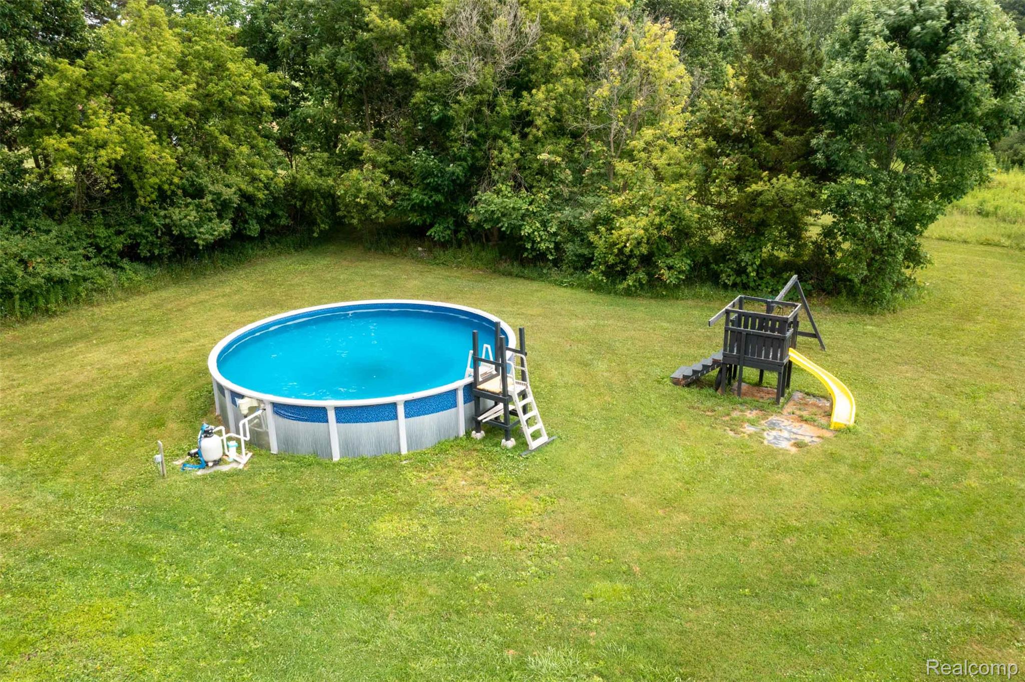 5761 Genesee Road Lapeer, MI 48446 - Photo 44 of 52 Expansive outdoor space featuring a large above-ground pool with a ladder, pool equipment, and a separate play structure with a slide