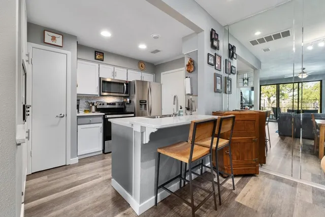 a kitchen with stainless steel appliances kitchen island granite countertop a refrigerator a stove a sink a dining table and chairs with wooden floor