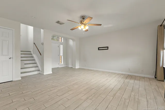 a view of an empty room with wooden floor and a ceiling fan