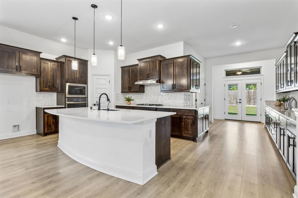 5224 Troupe Road McKinney, TX 75071 - Photo 12 of 31 Modern kitchen featuring a large central island with a solid surface countertop, dark wood-finish cabinetry, and light wood-finish flooring